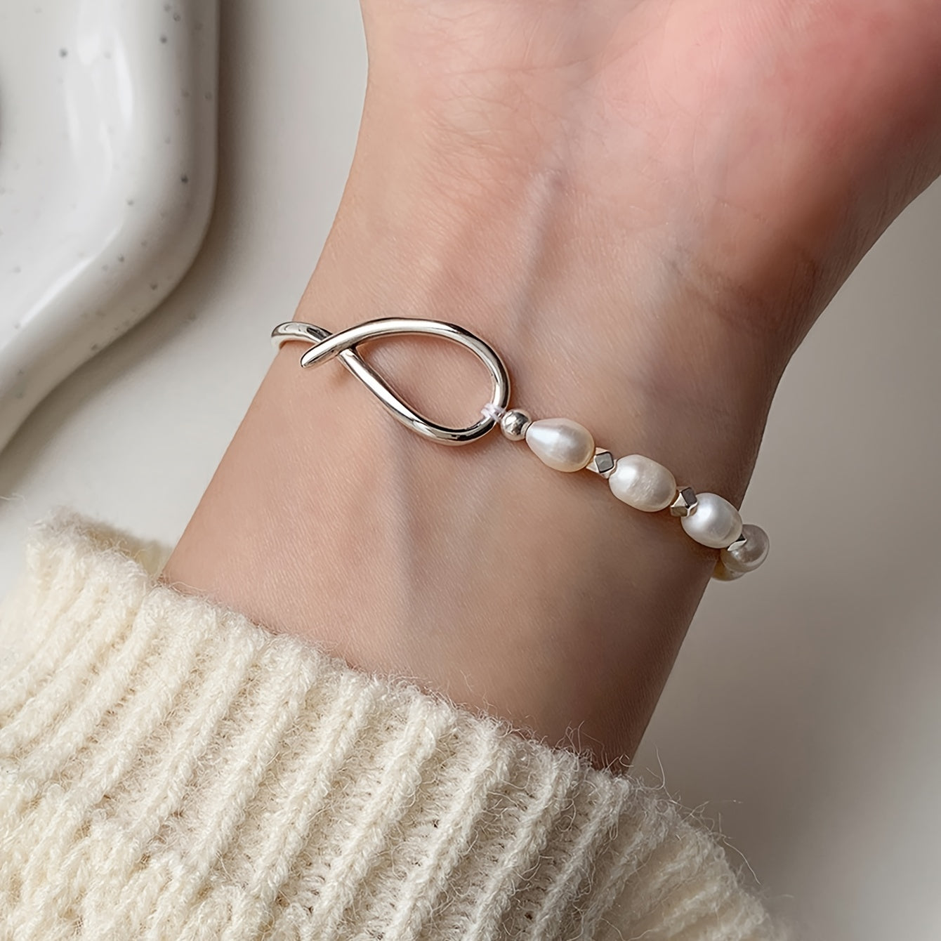 Silver bracelet with pearls on a wrist, wearing a beige sweater.